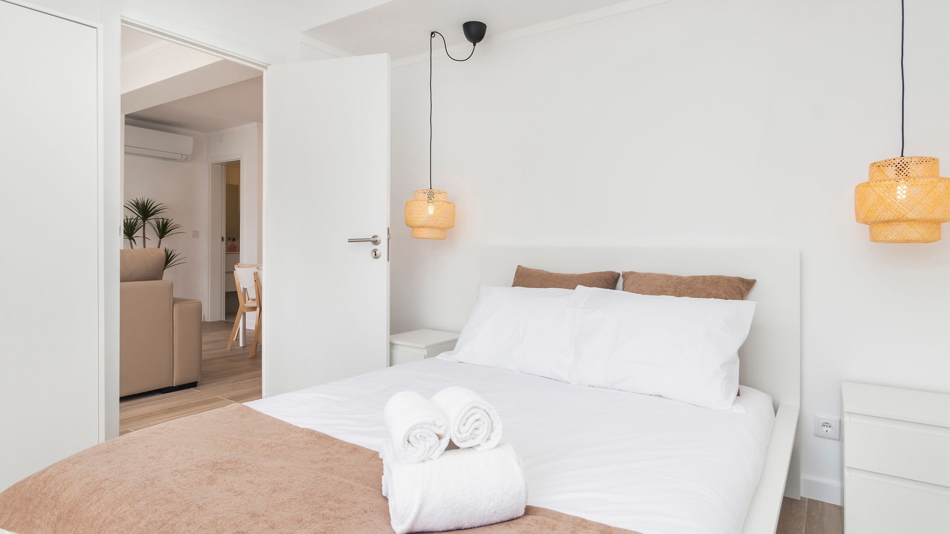 Ein modernes Schlafzimmer mit einem großen Bett, weißer Bettwäsche, Holzboden, einem kleinen Nachttisch und einer Hängeleuchte.