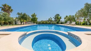 Una piscina con un diseño de mosaico azul turquesa, rodeada por un muro de piedra bajo y diversos árboles.