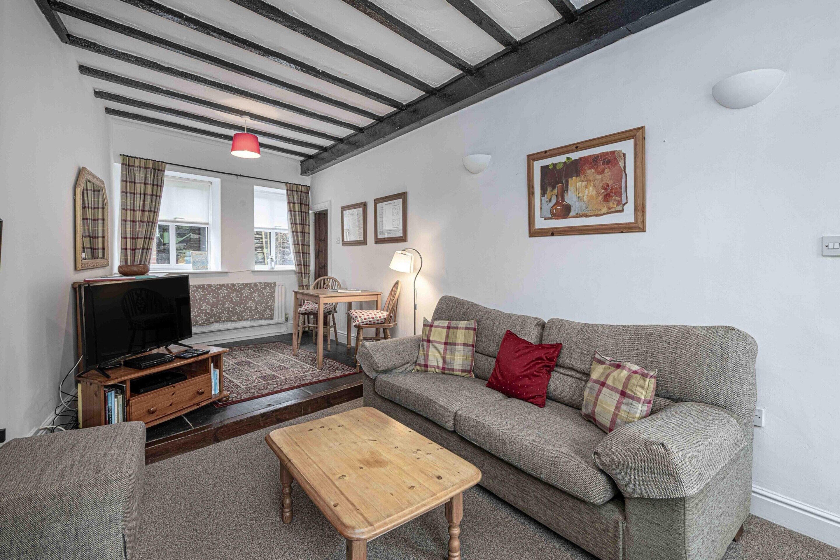 Un salon avec un canapé, une table basse en bois, un téléviseur posé sur un meuble en bois, une lampe et un tableau accroché au mur.