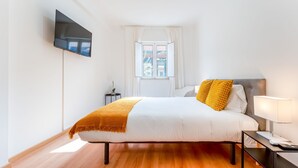 A modern bedroom with a bed, a TV mounted on the wall, a bedside table with a lamp, and a window with curtains. - Modern Retreat in Castro Marim by LovelyStay (Castro Marim)