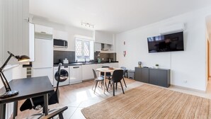 A modern kitchen with white cabinets, a dining area with a round table and chairs, a TV mounted on the wall, and a washing machine. - Modern Retreat in Castro Marim by LovelyStay (Castro Marim)