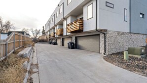 Un edificio moderno de varios pisos con fachada de hormigón, balcones con cajas de madera y una base de piedra.