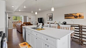 Una cocina moderna con armarios blancos, una isla grande, iluminación colgante y obras de arte en las paredes.