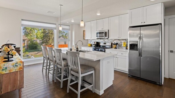Una cocina moderna con armarios blancos, electrodomésticos de acero inoxidable y una isla grande con taburetes de bar.