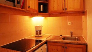 A compact kitchen with wooden cabinets, a built-in dishwasher, a coffee maker, and a sink. - Ski-in/ski-out & foot of the slopes, 2nd floor, swimming pool, sauna, balcony, tv, ski locker, 35m² (Les Orres)
