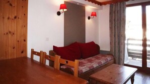 A cozy room with a wooden dining table, a sofa with red cushions, and two wall-mounted lamps. - Ski-in/ski-out & foot of the slopes, 2nd floor, swimming pool, sauna, balcony, tv, ski locker, 35m² (Les Orres)