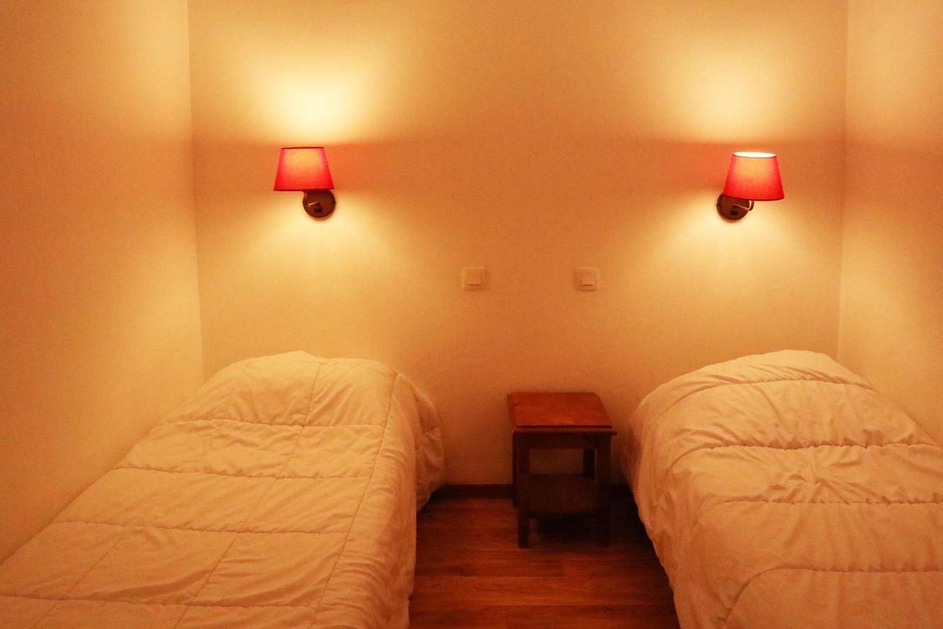 A small, dimly lit room with two single beds and a nightstand.