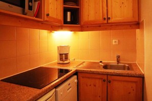 A compact kitchen with wooden cabinets, a built-in dishwasher, a coffee maker, and a sink.