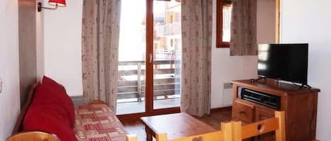A cozy room with a wooden sofa, a small table, a TV, and a balcony with curtains.