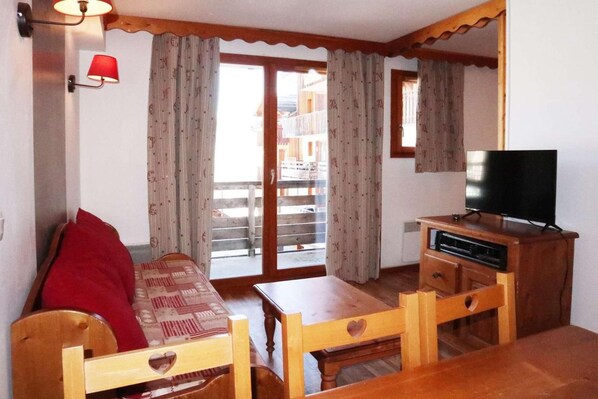 A cozy room with a wooden sofa, a small table, a TV, and a balcony with curtains.