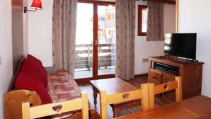 A cozy room with a wooden sofa, a small table, a TV, and a balcony with curtains. - Ski-in/ski-out & foot of the slopes, 2nd floor, swimming pool, sauna, balcony, tv, ski locker, 35m² (Les Orres)