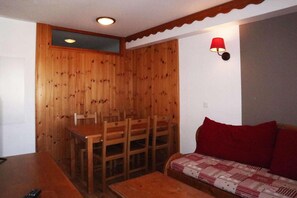A wooden dining area with a table and chairs, a red lamp, and a sofa with a patterned cover.