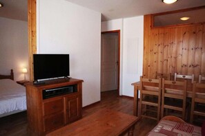 A room with a wooden TV stand, a bed, a dining table, and a set of wooden chairs.