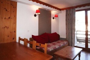 A cozy room with a wooden dining table, a sofa with red cushions, and two wall-mounted lamps.