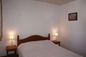 A single bed with a wooden headboard in a room with white walls. There are two bedside tables with lamps on either side of the bed.