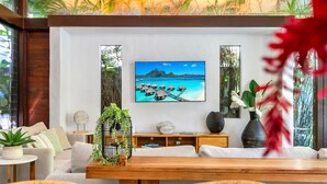 Un salon moderne doté d’un grand téléviseur à écran plat fixé au mur, d’une table basse en bois, d’un canapé et d’une table d’appoint agrémentée d’une plante.