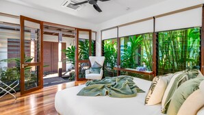 Une chambre spacieuse avec un grand lit, un fauteuil et une vue sur une végétation luxuriante, grâce à de grandes fenêtres.