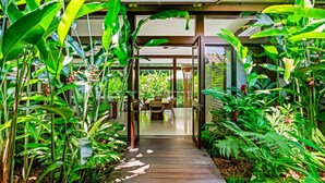 Un sentier en bois mène à un espace repas entouré d’une végétation tropicale luxuriante.