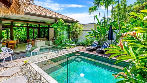 Un espace piscine extérieur moderne, doté de chaises longues, d’un coin repas et d’une végétation tropicale luxuriante.