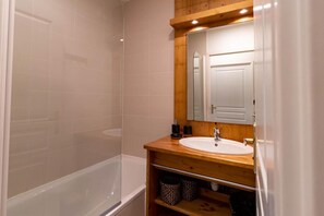 Ein Badezimmer mit Holz-Waschtisch, einem weißen Waschbecken, einem Spiegel und einer Duschkabine.