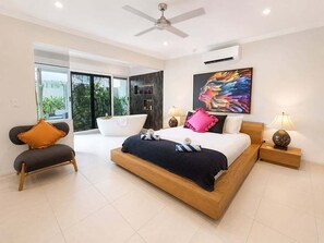 A modern bedroom with a large bed, a ceiling fan, a nightstand, and a window with a view.