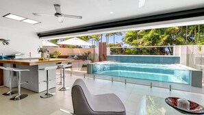 A modern kitchen with a bar area, a hot tub, and a poolside seating area with a view of palm trees.
