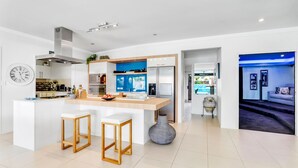 A modern kitchen with a central island, bar stools, a large vase, and a view into a living area with a pool.