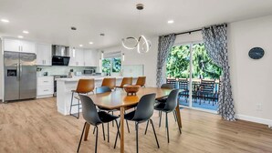 A modern kitchen with white cabinets, a stainless steel refrigerator, and a dining area with a wooden table and black chairs. - Lakefront Retreat for 6 with Stunning Views, Sauna (Snohomish)