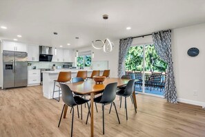 A modern kitchen with white cabinets, a stainless steel refrigerator, and a dining area with a wooden table and black chairs. - Lakefront Retreat for 6 with Stunning Views, Sauna (Snohomish)