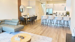 A modern living room with a sectional sofa, dining table, and bar stools. - TR17406SB - New 3BR Villa w/ Pool | 17min Disney (Clermont)