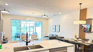 A modern kitchen with a central island, dining area with chairs and a table, and a seating area with a sofa. - TR17406SB - New 3BR Villa w/ Pool | 17min Disney (Clermont)