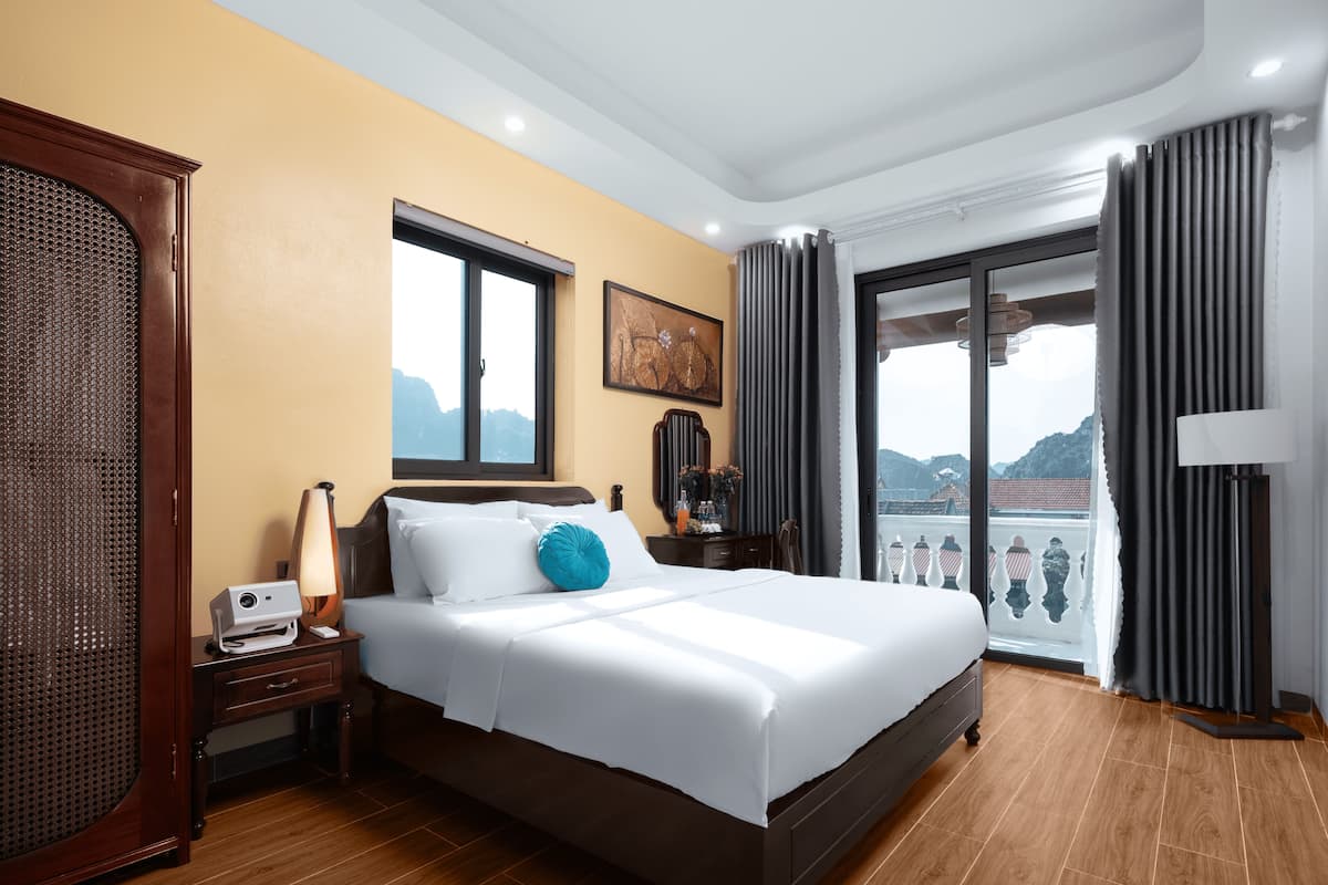 Une chambre d’hôtel avec un grand lit, une table de chevet en bois, un bureau, une chaise, une fenêtre donnant sur les montagnes et un balcon avec une balustrade.