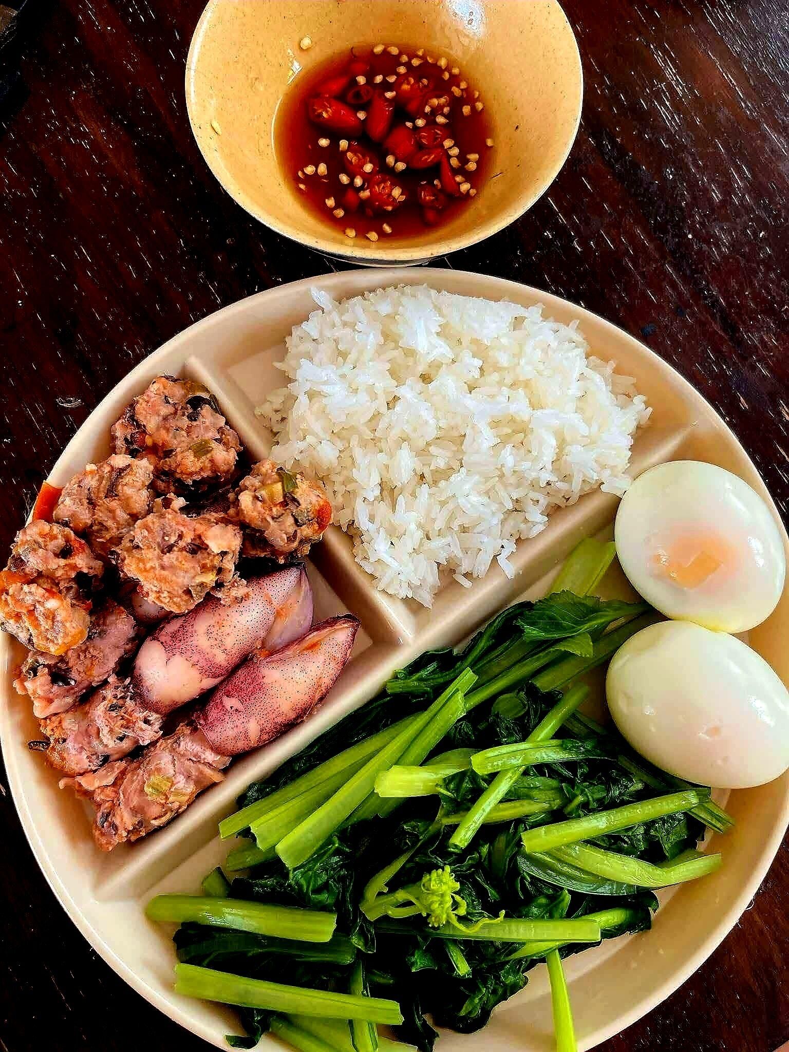 A meal consisting of rice, meat, vegetables, and eggs on a plate.