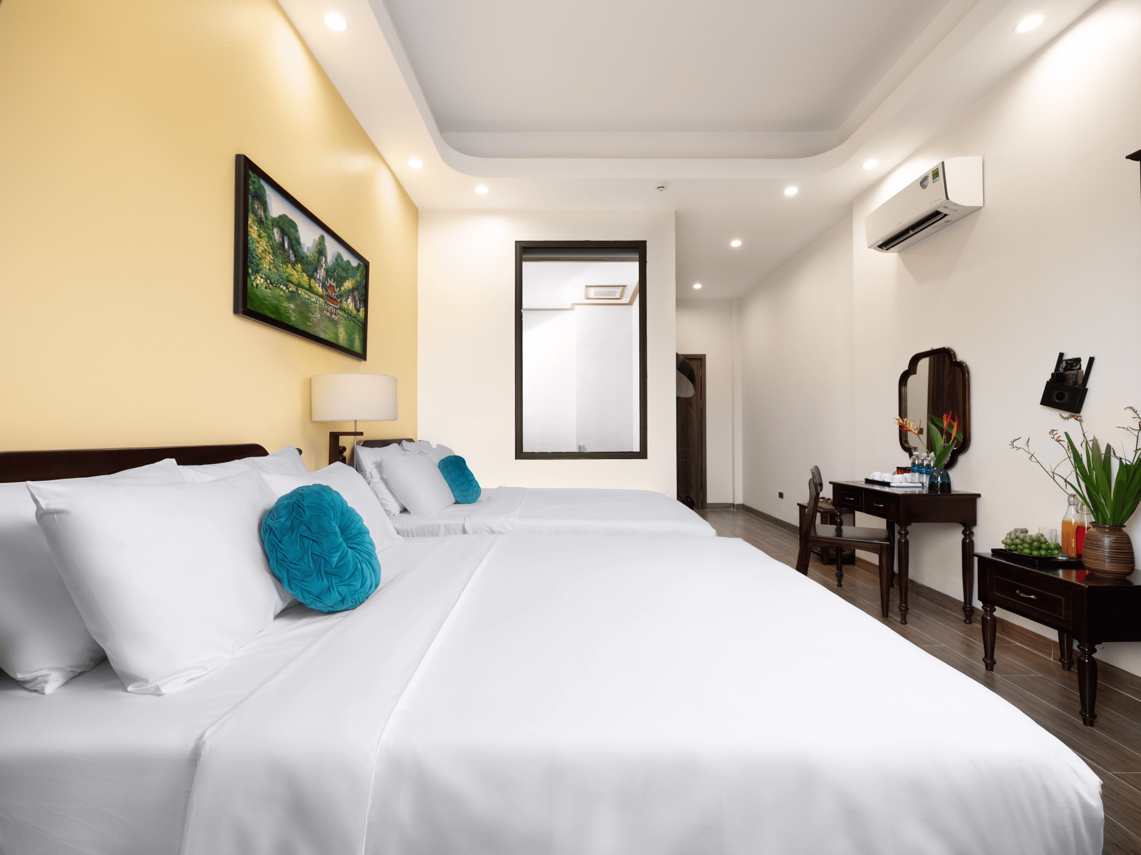 A hotel room with two beds, a desk, a chair, a mirror, a lamp, and an air conditioning unit.