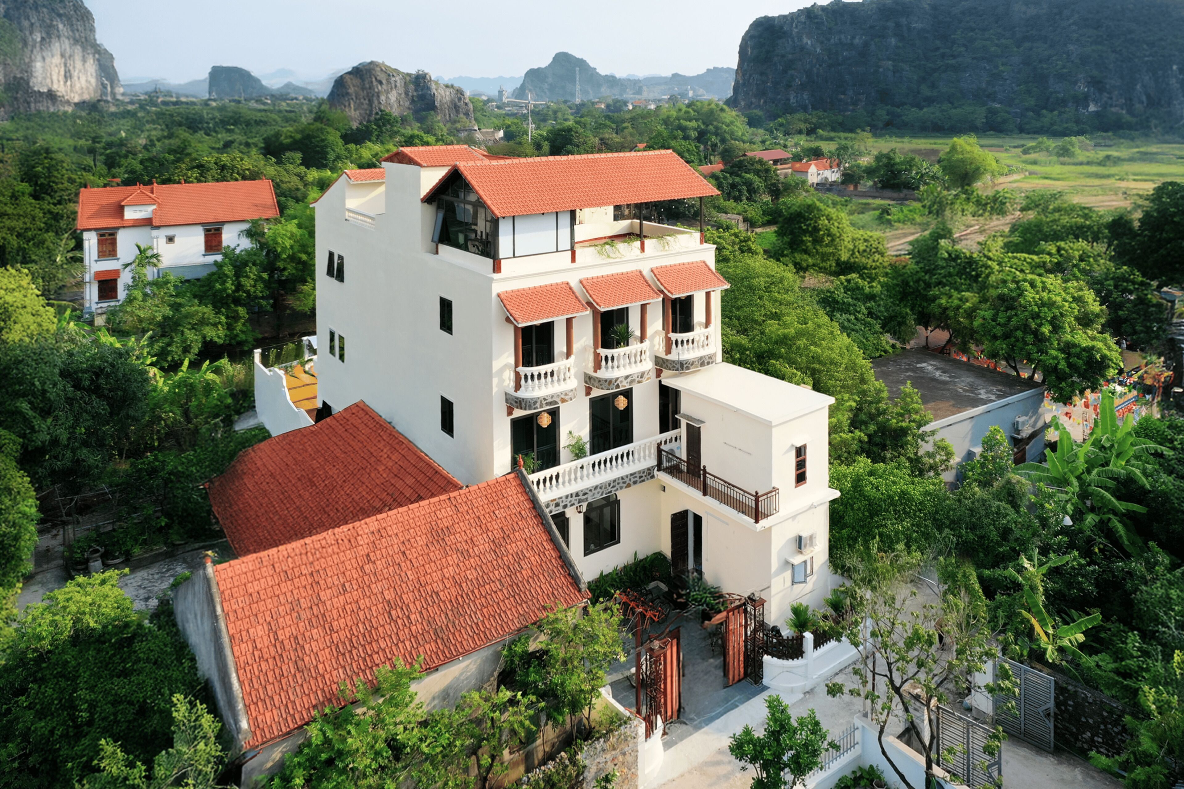 A multi-story building with a red-tiled roof, surrounded by lush greenery and mountains in the background.