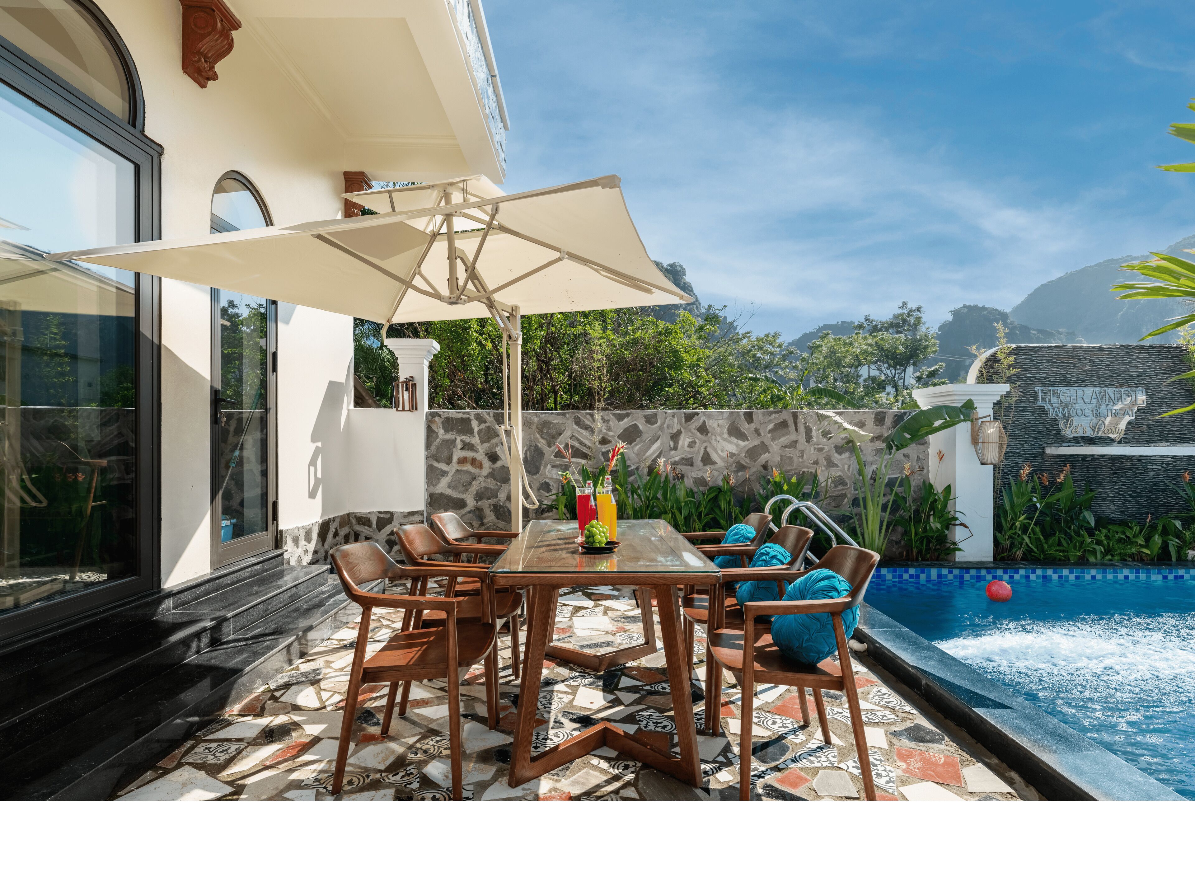 An outdoor dining area with a table and chairs, a large umbrella, and a pool.