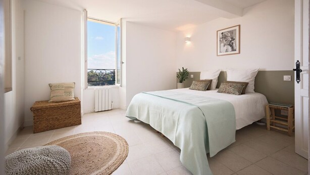 Un dormitorio con cama, ventana, radiador, una mesita y una cesta.