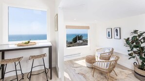 Une cuisine moderne dotée d’une grande fenêtre donnant sur la mer, d’un coin bar avec des tabourets et d’un espace salon avec vue.