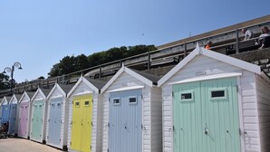 A row of colorful beach huts with numbered doors, a staircase leading to a viewing platform, and a clear sky. - Willow's Leap (Lyme Regis)