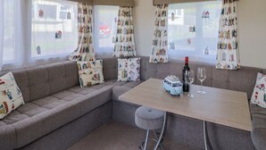 A cozy room with a sofa, a small table, and a bar stool. There are curtains with a nautical theme, and a bottle of wine on the table. - Willow's Leap (Lyme Regis)