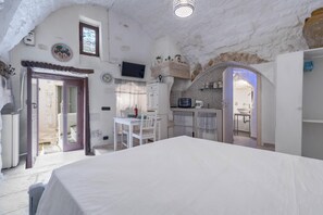 A room with a bed, a dining table with chairs, a kitchen area, and a bathroom visible through an archway.