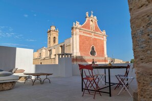 Eine Terrasse im Freien mit Tisch und Stühlen, einer Steinsitzbank und Blick auf eine historische Kirche mit Glockenturm.