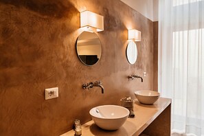 A bathroom with two round mirrors, a beige sink, and a wall-mounted light fixture. - Palazzo Pati - Suite Deluxe (Tiggiano)