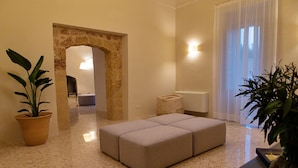 A modern living room with a stone archway, a beige sectional sofa, and a potted plant. - Palazzo Pati - Suite Deluxe (Tiggiano)