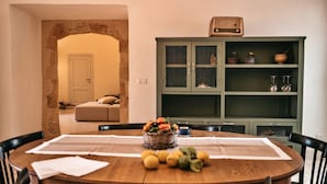 A dining area with a round wooden table set for four, surrounded by chairs. A basket of fruit and a bowl of lemons are on the table. - Palazzo Pati - Suite Deluxe (Tiggiano)