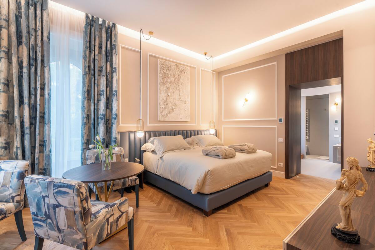 Une chambre d’hôtel moderne avec un grand lit, une table ronde et un coin salon doté de fauteuils rembourrés.