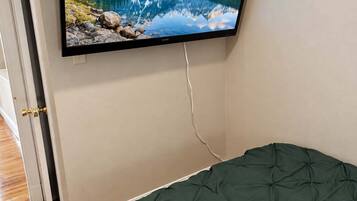 A bedroom with a bed, a wall-mounted TV displaying a mountain landscape, and a door leading to another room.