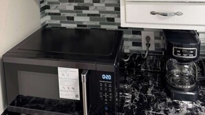 A kitchen with a microwave, coffee maker, and shelves with glass jars and white bowls. - 3BR King Beds | 85” TV | 4min to A&T & Downtown (Greensboro)