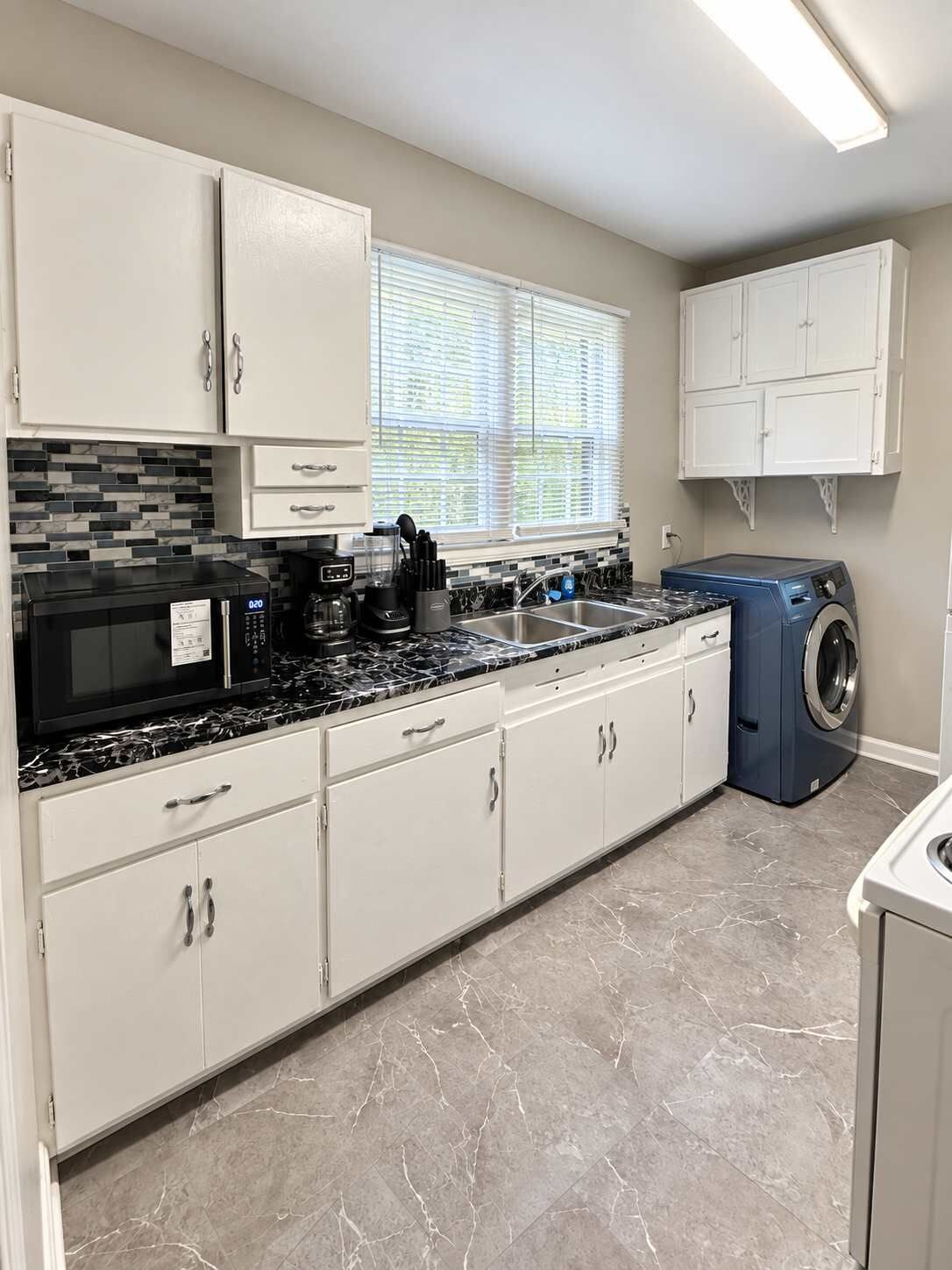 A modern kitchen with white cabinets, a black countertop, and a built-in washing machine.
