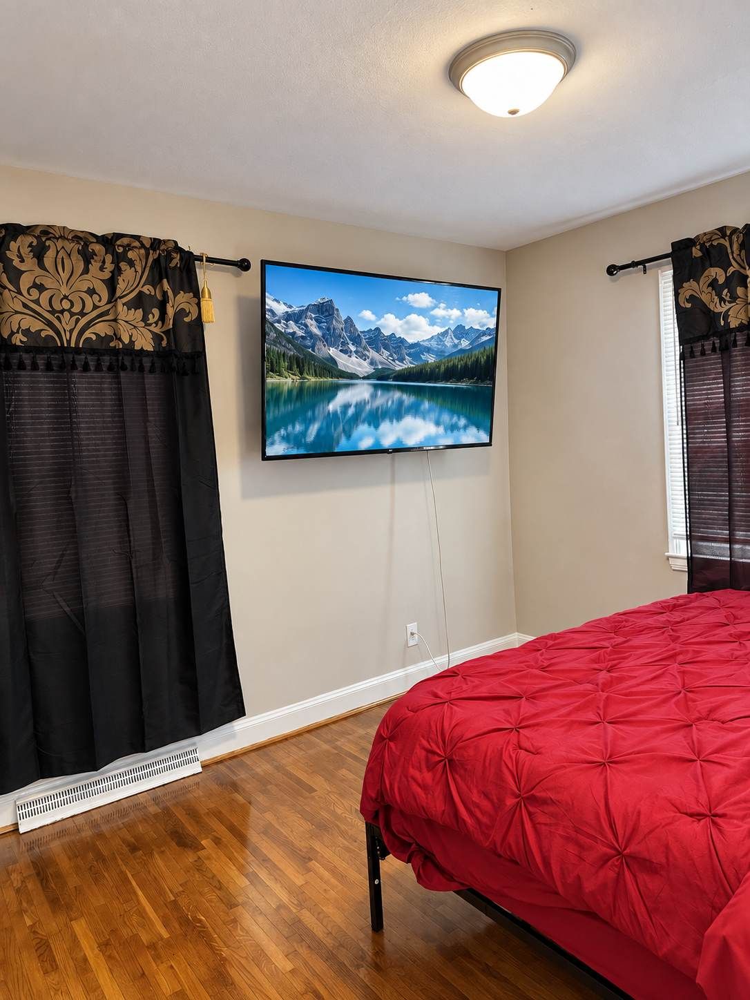 A bedroom with a bed, a television mounted on the wall, and a window with curtains.